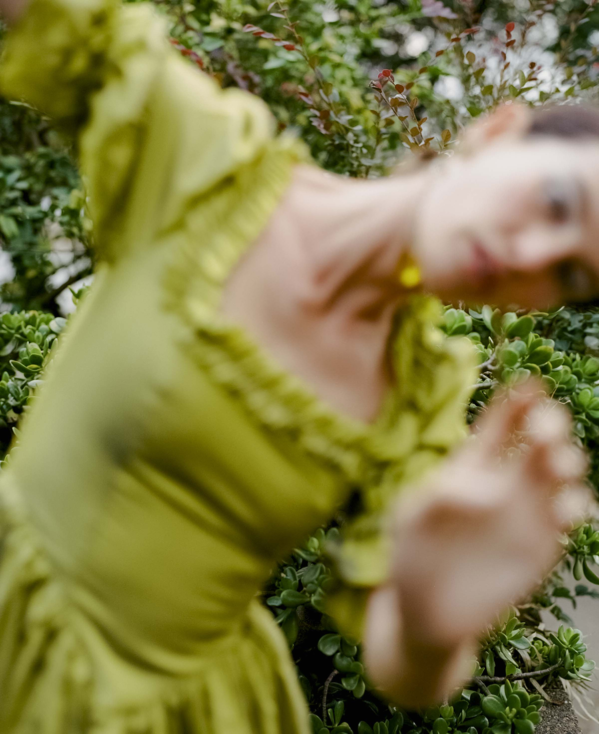 Woman in a lime-green historical dress posing in a garden, background of blurred foliage and leaves, shallow depth of field.