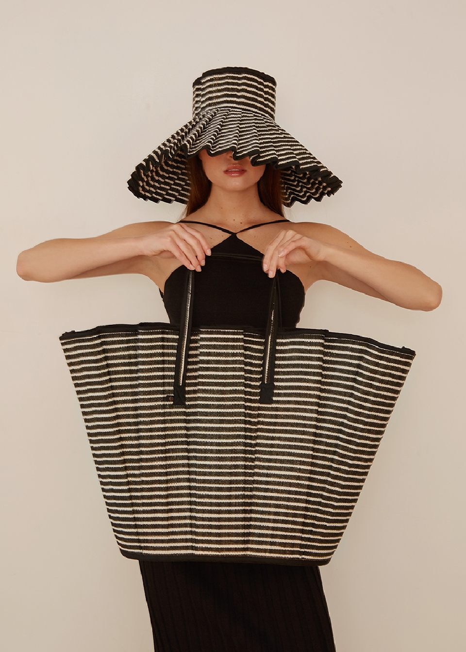 Woman wearing striped sun hat and holding a large striped tote bag. Studio shot with a neutral background. Fashion and style.