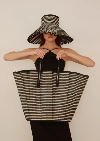 Woman wearing striped sun hat and holding a large striped tote bag. Studio shot with a neutral background. Fashion and style.