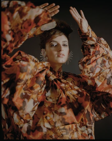 Woman in floral print blouse with puffed sleeves raising hands near her face with starburst earrings by Natasha Killeen