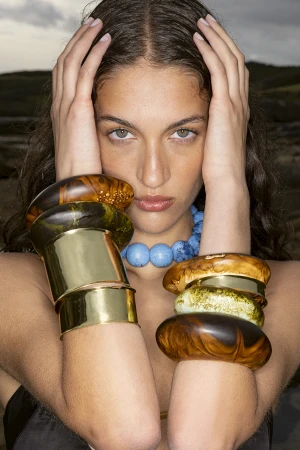 Close-up portrait of a woman holding her head with hands displaying chunky resin bangles and gold cuffs