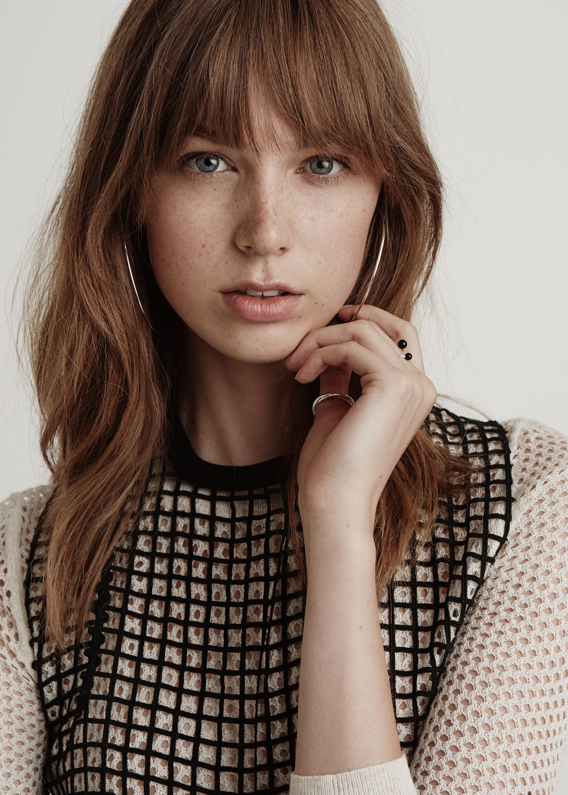 Close-up portrait of an adult woman with brown hair and freckles wearing a patterned top against a white background.