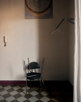 Minimalist interior featuring an overturned chair, artwork, and checkerboard floor in a room with neutral walls and warm lighting.
