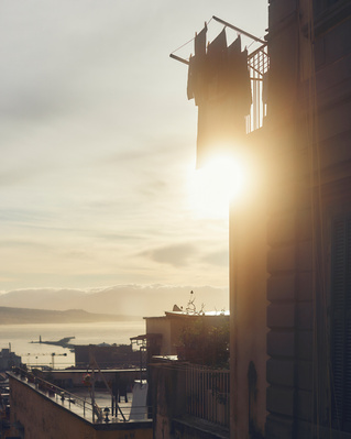 Scenic view of laundry drying on a line outside a building with a city and the sea in the distance during golden hour.