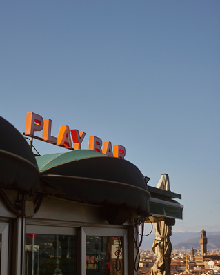 Outdoor shot of the PLAY BAR sign above a dark green awning and white trim, set against a blue sky in Florence, Italy.
