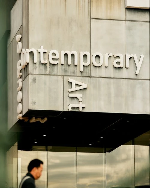 Exterior of the Contemporary Art museum featuring an adult pedestrian walking in front of the mirrored glass windows.
