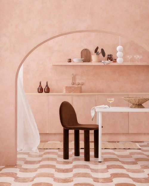 Interior design featuring a brown chair by a white table, with pale pink walls, rounded doorway, and patterned floor tiles.