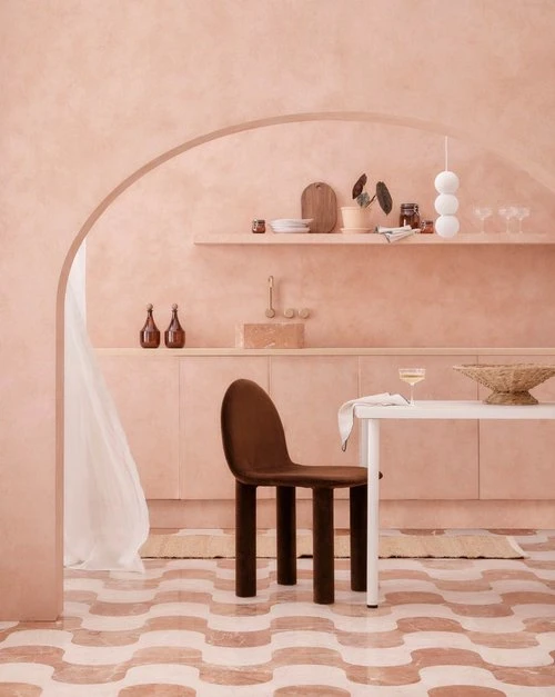 Interior design featuring a brown chair by a white table, with pale pink walls, rounded doorway, and patterned floor tiles.