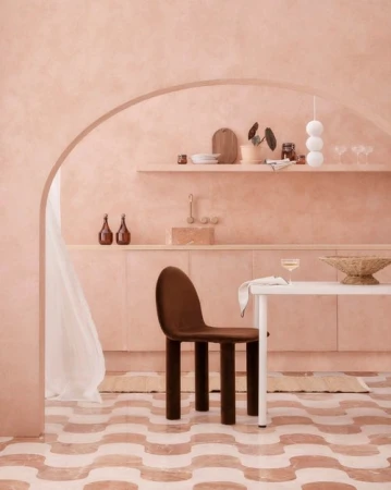 Interior design featuring a brown chair by a white table, with pale pink walls, rounded doorway, and patterned floor tiles.