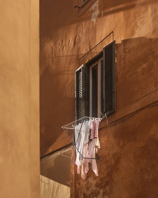 Exterior of a building with a window and dark shutters, illuminated at night. Clothes hang on a drying rack outside the window.