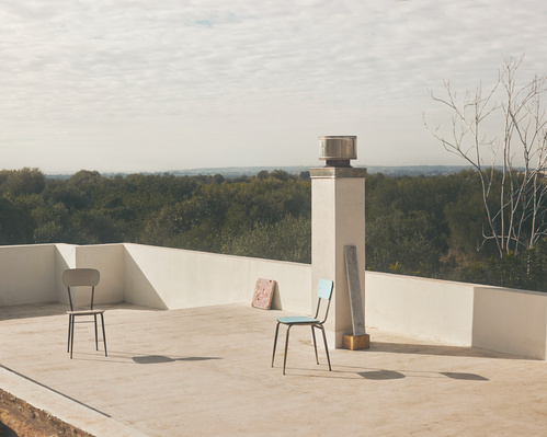 Outdoor rooftop scene with two chairs, a chimney, and a distant forest backdrop under a cloudy sky, creating a minimalist composition.
