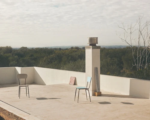 Outdoor rooftop scene with two chairs, a chimney, and a distant forest backdrop under a cloudy sky, creating a minimalist composition.