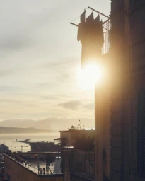 Laundry hanging on a balcony railing against a bright sun flare over urban rooftops at sunset