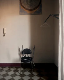 An upturned black metal chair resting on a matching chair in a corner of an interior room with patterned floor tiles.