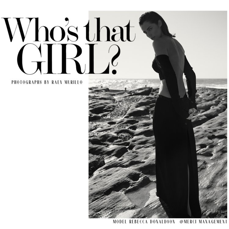 A fashion editorial shot in black and white featuring a young adult female model in a long skirt and arm coverings on a rocky beach.