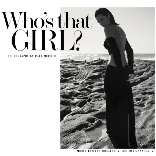A fashion editorial shot in black and white featuring a young adult female model in a long skirt and arm coverings on a rocky beach.