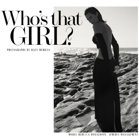 A fashion editorial shot in black and white featuring a young adult female model in a long skirt and arm coverings on a rocky beach.