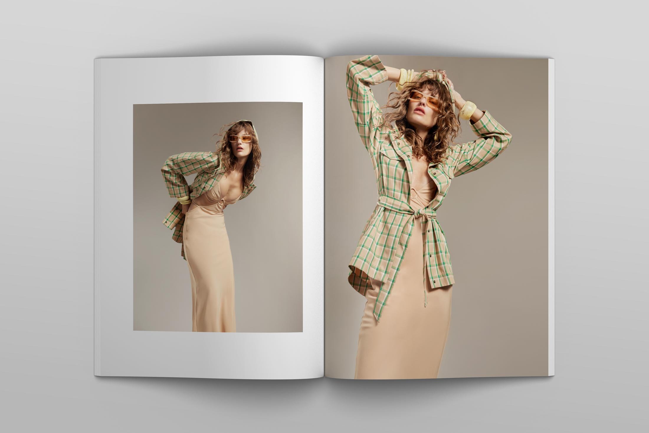 Fashion editorial photograph in an open magazine featuring a woman in a plaid shirt and dress, posing with a neutral background.