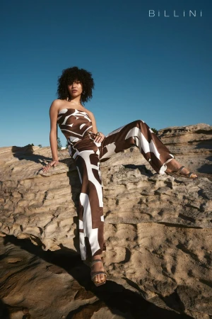 A model poses on a rock wearing a brown and white patterned outfit with the sky in the background, creating a fashion forward image.