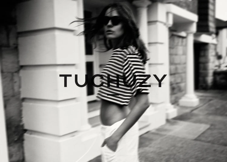 Woman in striped crop top and white pants poses near a building. Fashion shot features black and white tones, sunglasses, and streetwear.