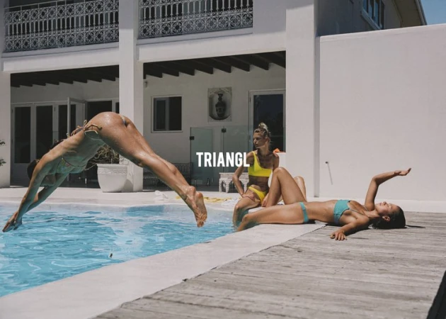 Three adult females in swimsuits near a pool; one is diving in the pool, the others are sunbathing by a modern white villa.