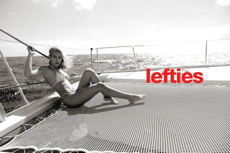 Blonde woman in a bikini relaxing on the netting of a yacht at sea under an open sky by photographer Raex Murillo.