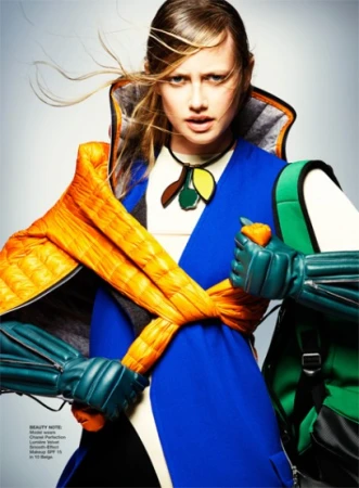 Fashion photo shoot features a woman in a blue dress with orange puffy sleeves and green gloves, set against a light grey background.