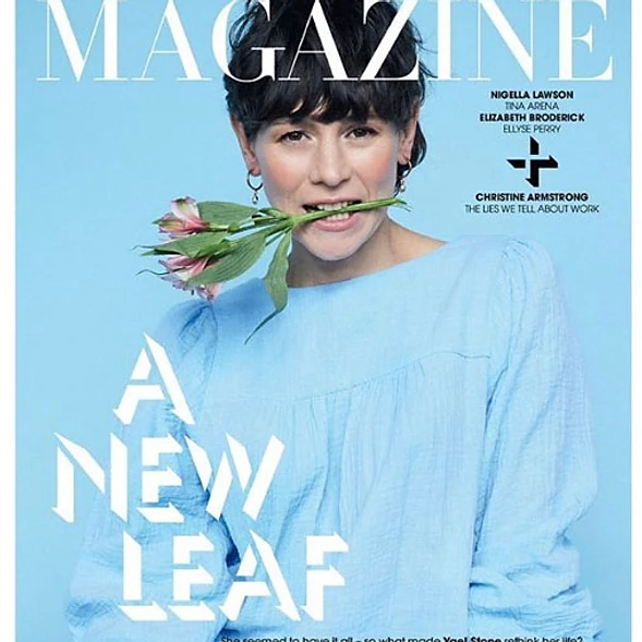Magazine cover featuring a woman with short dark hair holding a flower in her mouth, wearing a light blue top, against a light blue background.