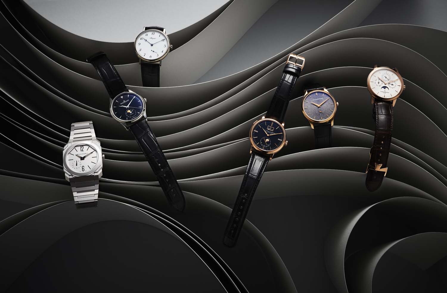 Product shot of a collection of wristwatches in a studio setting, arranged on a black and gray, wave-patterned surface.