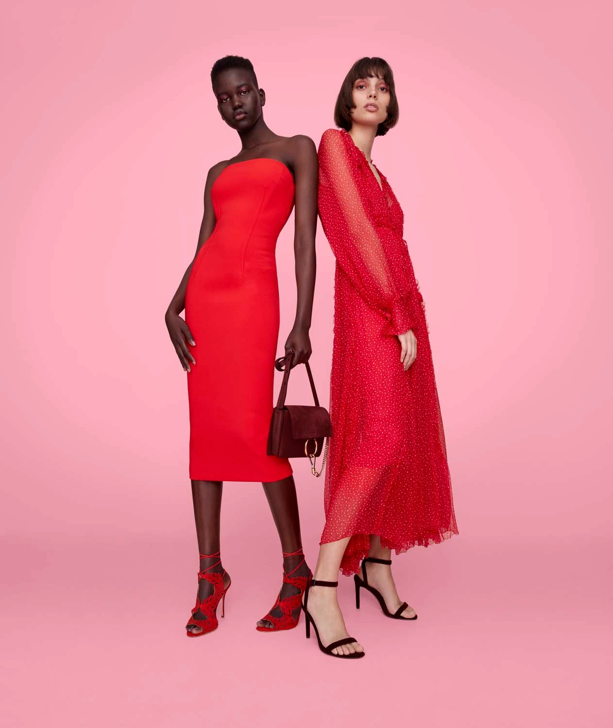 Two female fashion models in red dresses posing against a solid pink background, with retouched finish by Enrico Mezzi.