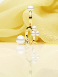 Golden rings adorned with white pearls and small diamonds displayed on a reflective surface against a draped yellow fabric.
