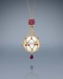 Close-up jewellery product image of an ornate gold necklace pendant featuring a large white pearl in a netted gold setting with rubies and emeralds.