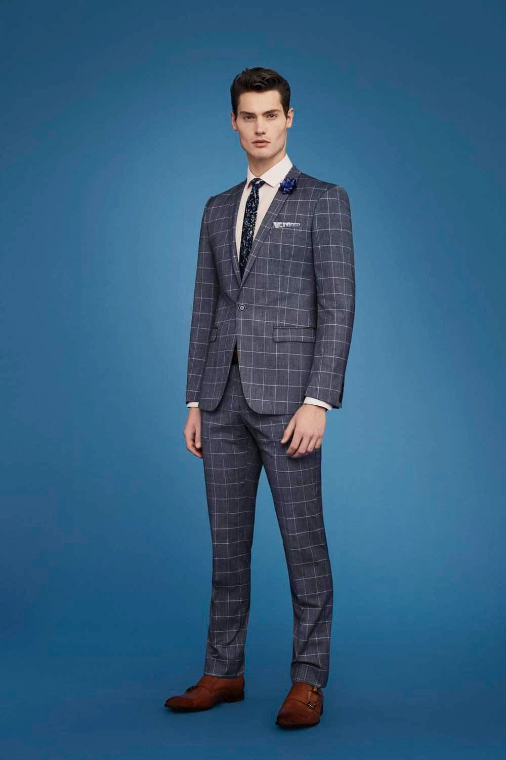 Full-length portrait of a man in a blue plaid suit and brown shoes against a blue background