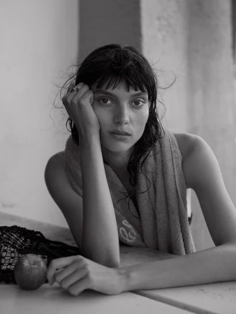 Monochrome portrait of a woman resting her head on her hand with a towel draped over her shoulder and an apple on the table.