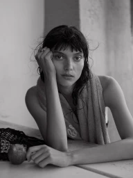 Monochrome portrait of a woman resting her head on her hand with a towel draped over her shoulder and an apple on the table.