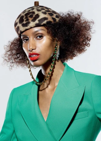 Close-up of a model wearing a leopard-print beret, vibrant green blazer, and gold chain earrings with red lipstick.
