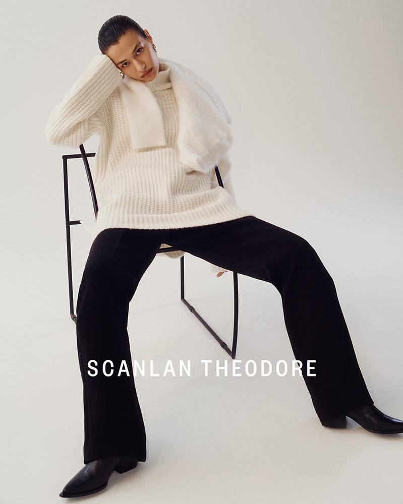Fashion shot of a slender adult posing in an oversized sweater, wide-leg pants, and leather boots. Studio lighting and simple background.