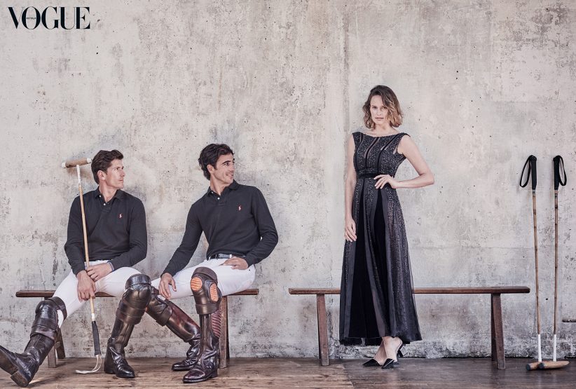 Fashion editorial featuring two polo players seated in riding attire alongside a woman in an elegant black evening gown, Vogue magazine backdrop.
