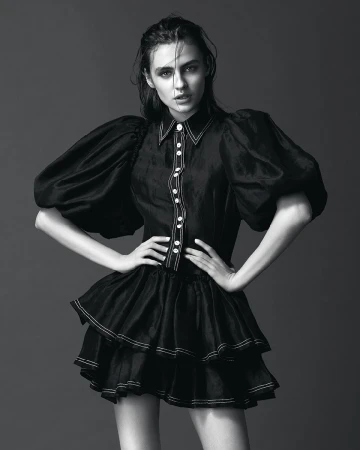 Model with dark wet-look hair wearing a black dress with voluminous puff sleeves and white contrast stitching.