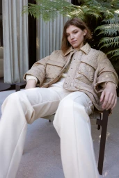 Woman seated in an outdoor chair wearing a quilted beige jacket and white trousers, styled by Nicole Adolphe.