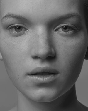 Close-up studio portrait of a young Caucasian woman with freckles, shot in black and white with even lighting and neutral background.