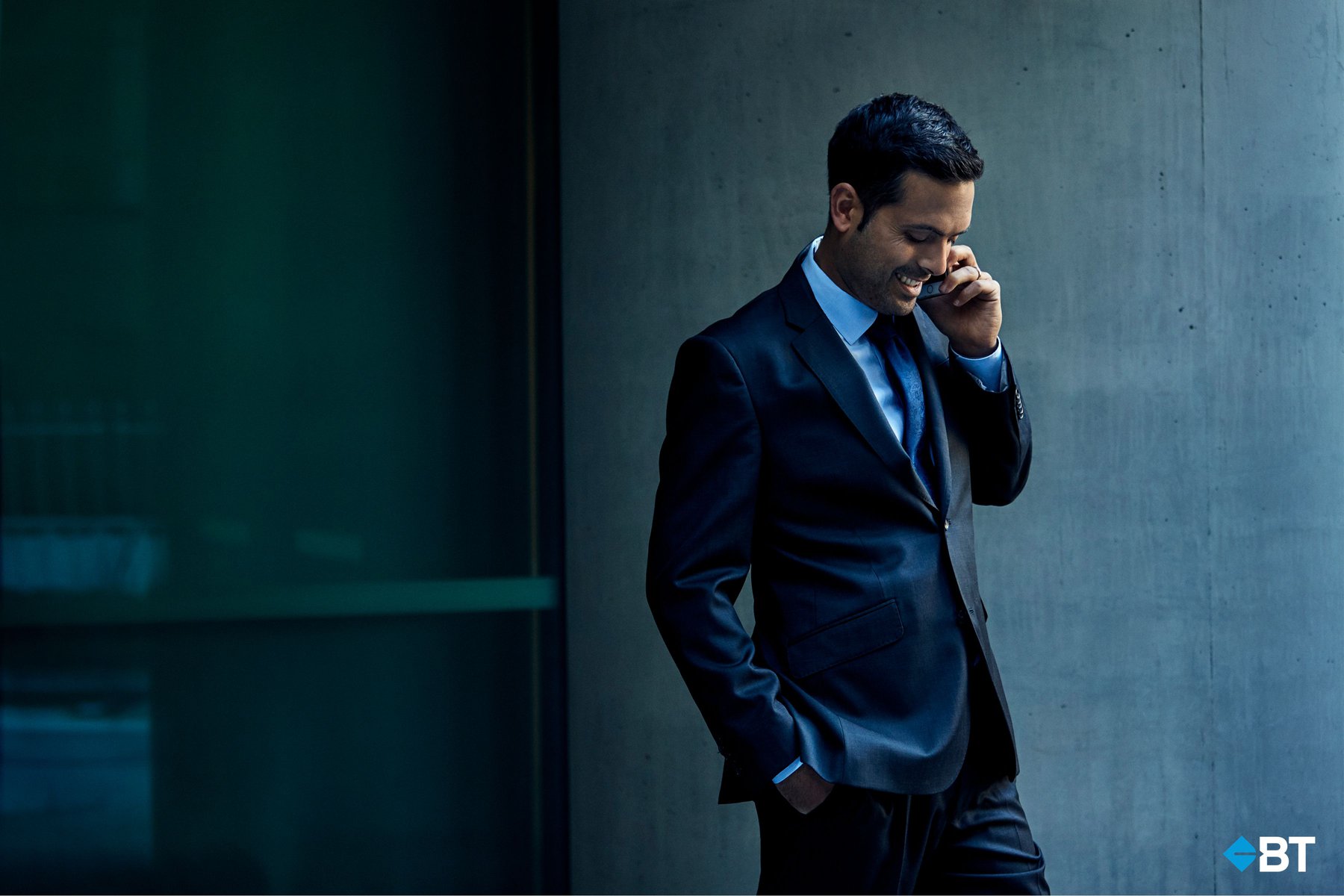 Smiling businessman in a suit uses a smartphone outdoors against a modern architectural backdrop, showcasing technology and professional life.