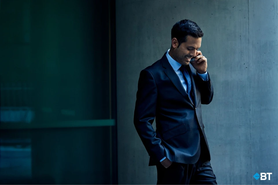 Smiling businessman in a suit uses a smartphone outdoors against a modern architectural backdrop, showcasing technology and professional life.