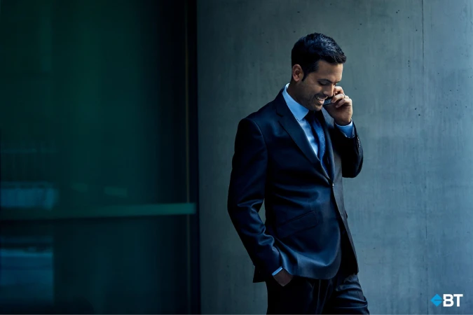 Smiling businessman in a suit uses a smartphone outdoors against a modern architectural backdrop, showcasing technology and professional life.