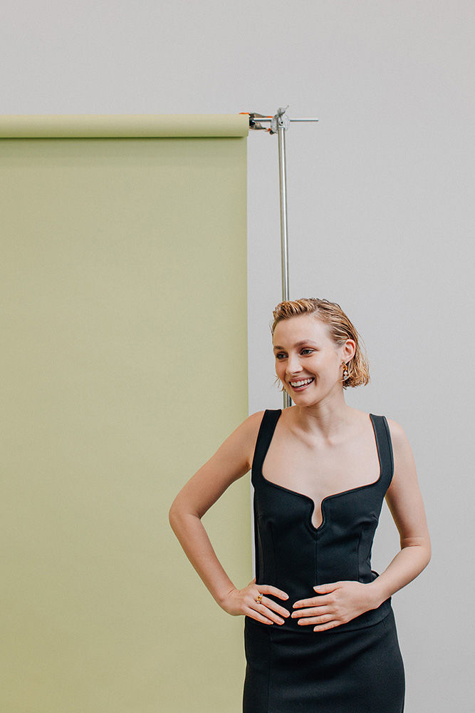 Woman with short wet hair wearing a black sleeveless top posing against a green backdrop with a metal stand