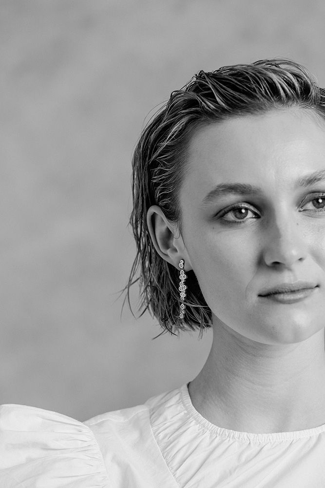Monochrome portrait of a woman with wet hair and a drop earring wearing a white top against a textured background.