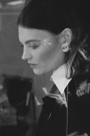 Black and white portrait of a woman wearing statement earrings and a dark blazer with a white collared shirt.
