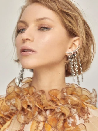 Close-up portrait of a woman with metallic silver eyeliner and cascading chain ear cuffs wearing a ruffled patterned top