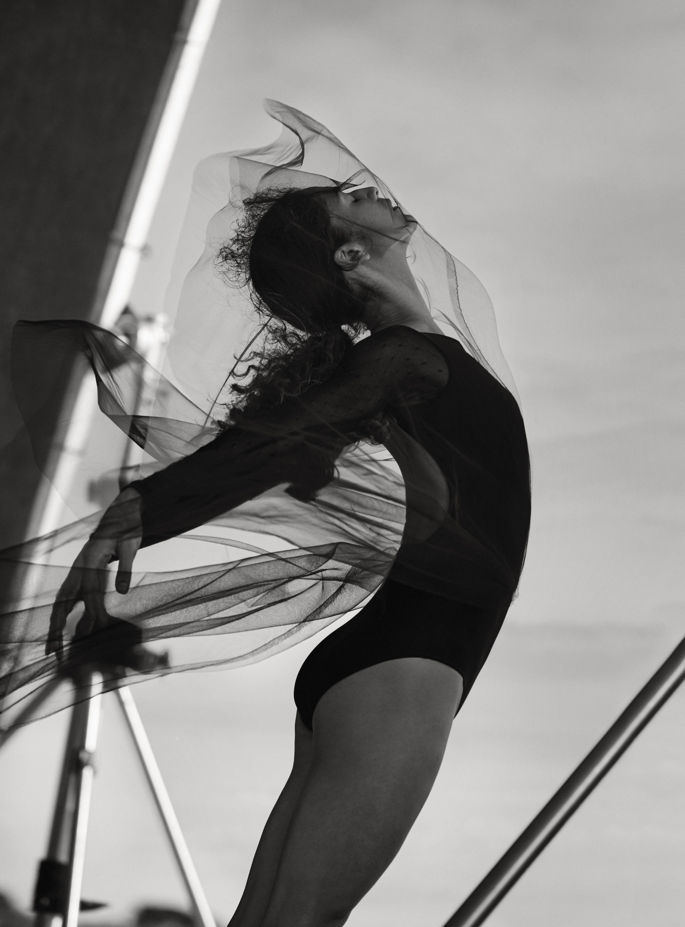 Monochrome studio shot of a graceful woman in a black bodysuit, elegantly posed with a sheer black veil, showcasing a dance-like motion.
