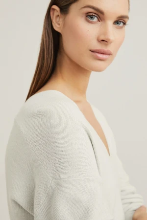 Close-up portrait of a woman with sleek brown hair and light grey top against a neutral background